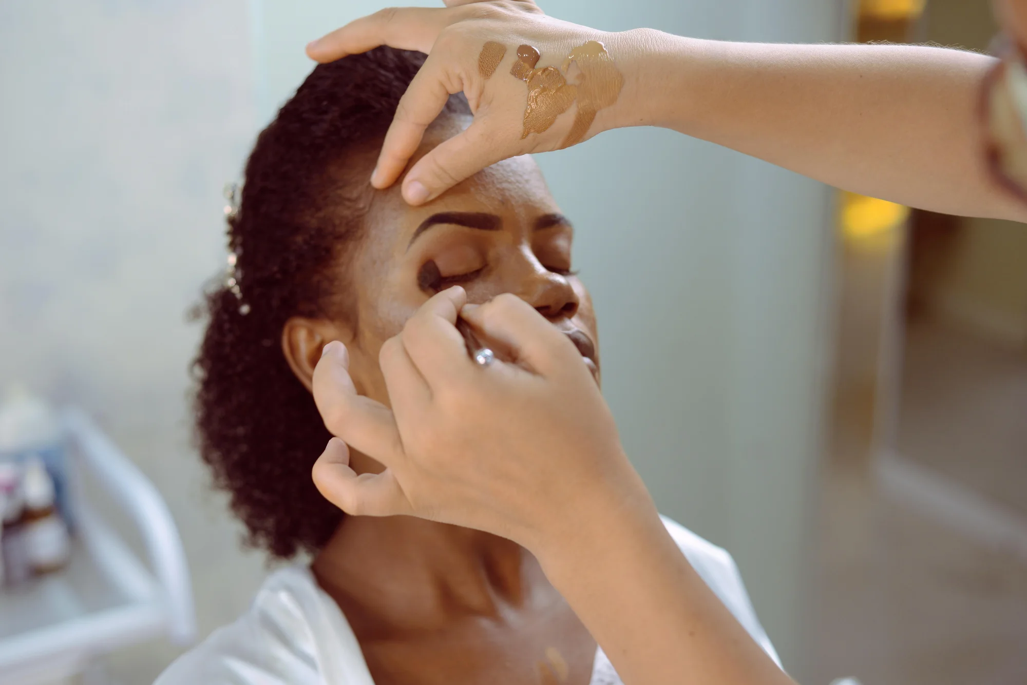 Makeup artist applying eyeshadow to a Black beauty client during event preparation